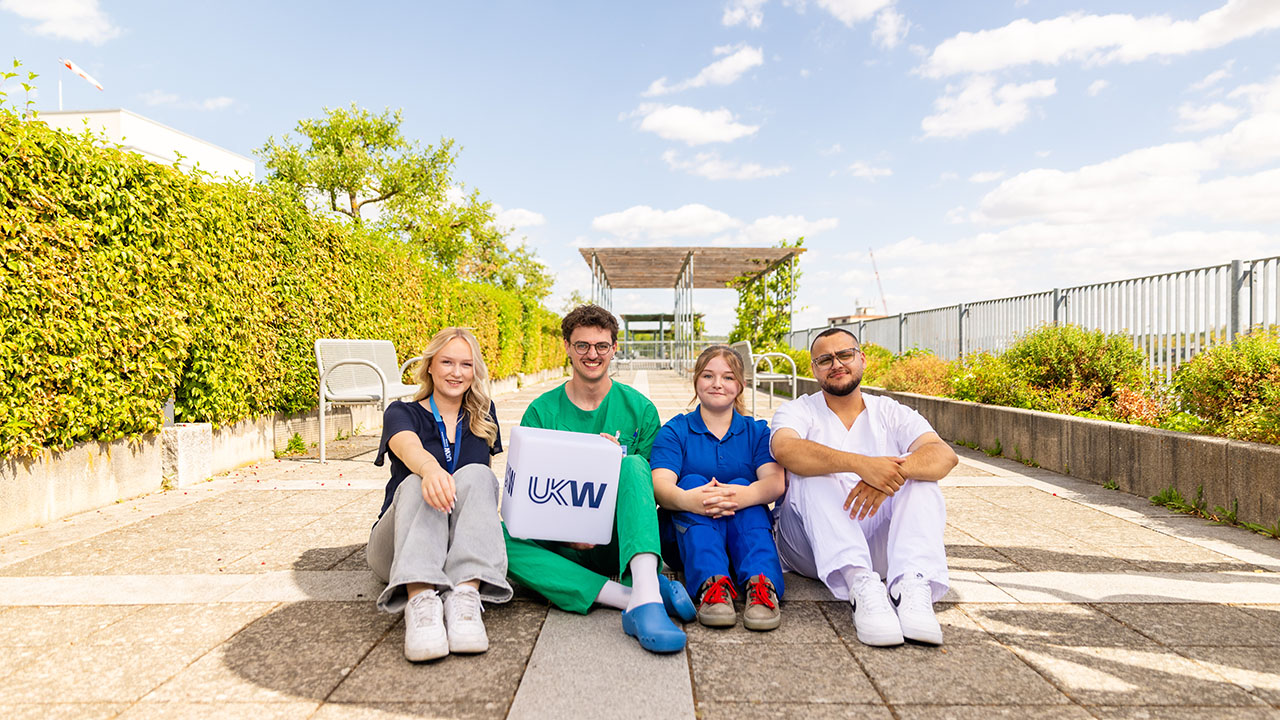 4 junge Mitarbeitende des Universitätsklinikum Würzburg die in Ihrer jeweiligen Arbeitskleidung 