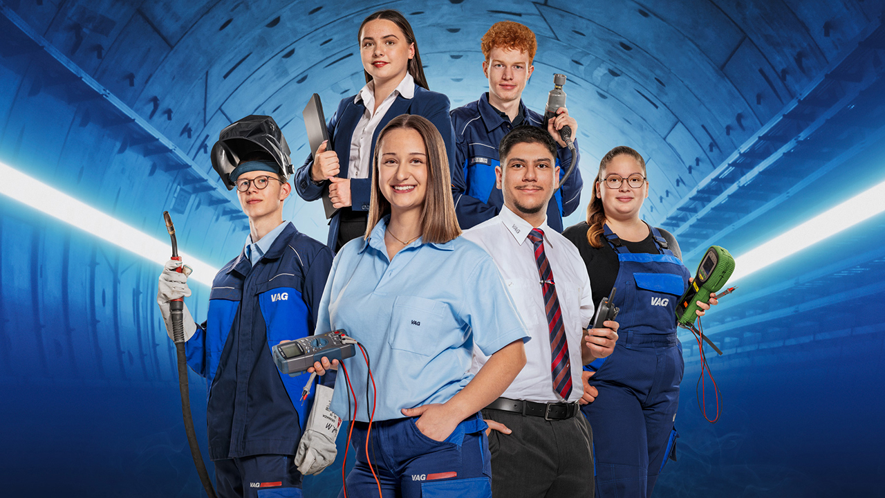 Sechs Auszubildende in ihrer jeweiligen Berufskleidung mit Werkzeugen bzw. Equipment aus ihren Berufen vor einem futuristisch anmutenden Hintergrund.