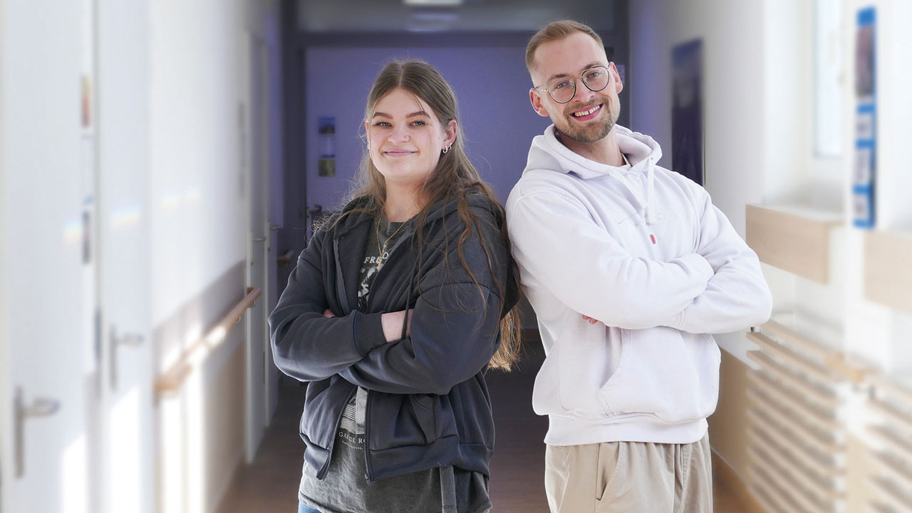 Zwei junge Menschen im Flur lachen in die Kamera