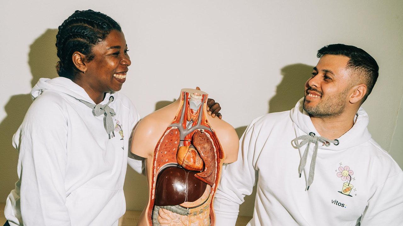 Zwei Personen lachen sich an, in der Mitte zwischen ihnen steht ein Modell eines menschlichen Oberkörpers