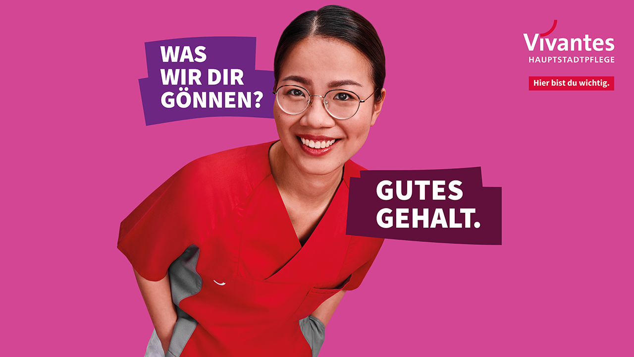 Lächelnde Person mit Brille in roter Pflegebekleidung vor einem pinkfarbenen Hintergrund, Bildaufschrift: Was wir dir gönnen? Gutes Gehalt.