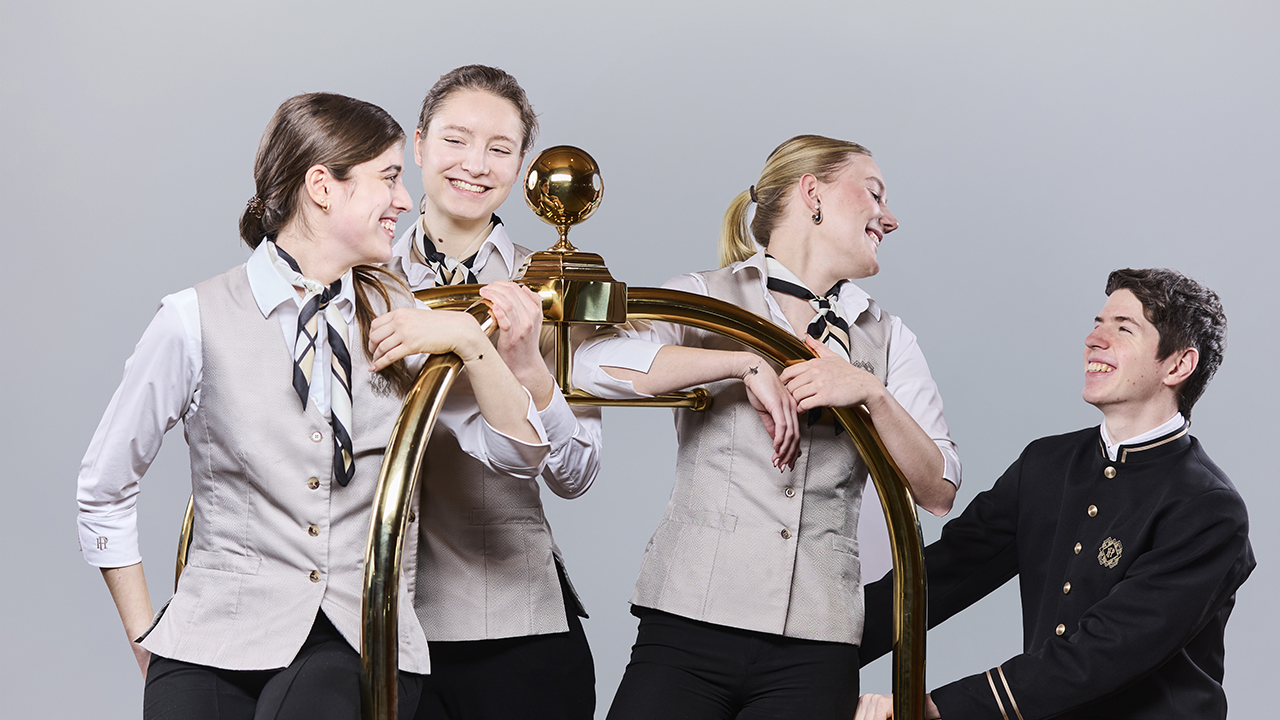 Vier Personen stehen um einen Gepäckwagen herum und lächeln sich gegenseittig an.