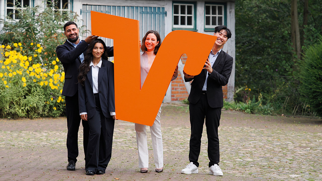 Vier Auszubildende mit einem großen orangefarbenen V in der Hand