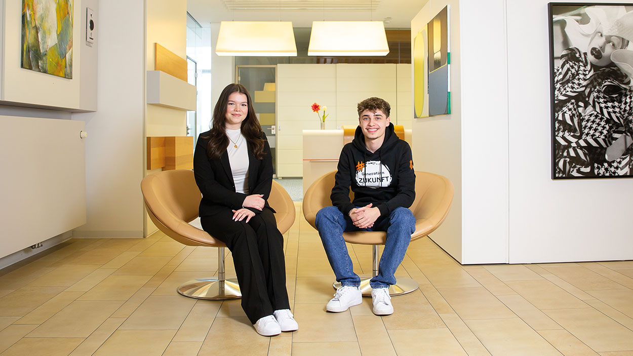 Zwei Personen sitzen auf einem Stuhl und blicken freundlich in die Kamera