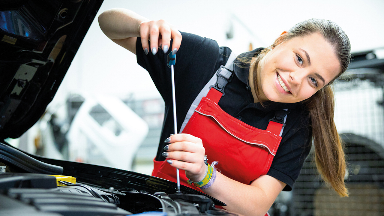 Junge Frau schraubt an Motor und lächelt in die Kamera