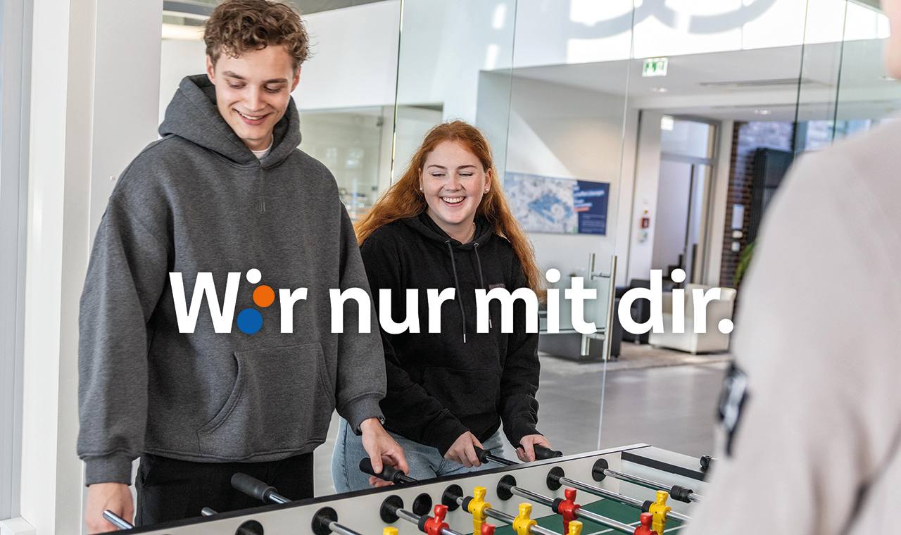 Zwei junge Menschen an einem Tischkickertisch, lachend. In der Mitte des Bildes der Schriftzug "Wir nur mit dir".