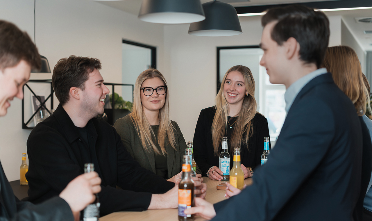 Gruppe von Menschen an einem Tisch, lachend, mit Getränken