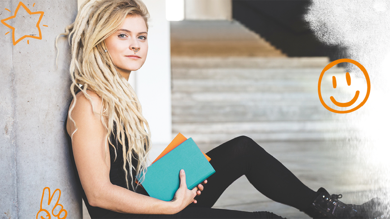 Junge Frau sitzt mit dem Rücken an eine Wand gelehnt mit ausgestreckten Beinen auf dem Boden. Sie hält zwei Hefte in der Hand. Per Graphik sind ein Stern ein Viktory-Zeichen und ein Smilay über das Bild gelegt. Die Frau lächelt.