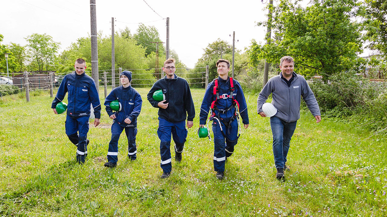 Fünf Personen in Arbeitskleidung gehen über eine Wiese. 