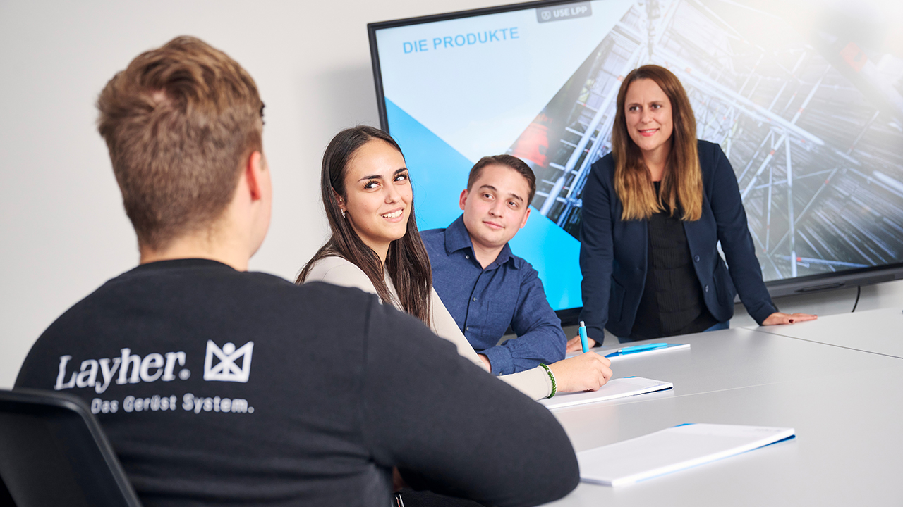 Drei Personen sehen in die Kamera, eine ist mit dem Rücken der Kamera zugewandt auf dem Pullover ist das Logo der Firma abgedruckt.