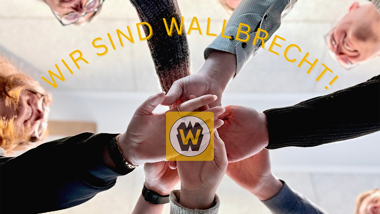 7 junge Menschen halten jeweils einen Arm in die Mitte. Die Hände berühren sich, das Foto ist von unten aufgenommen. Unter den Händen sieht man das Logo von Wilhelm Wallbrecht. Darüber der Slogan: Wir sind Wallbrecht!