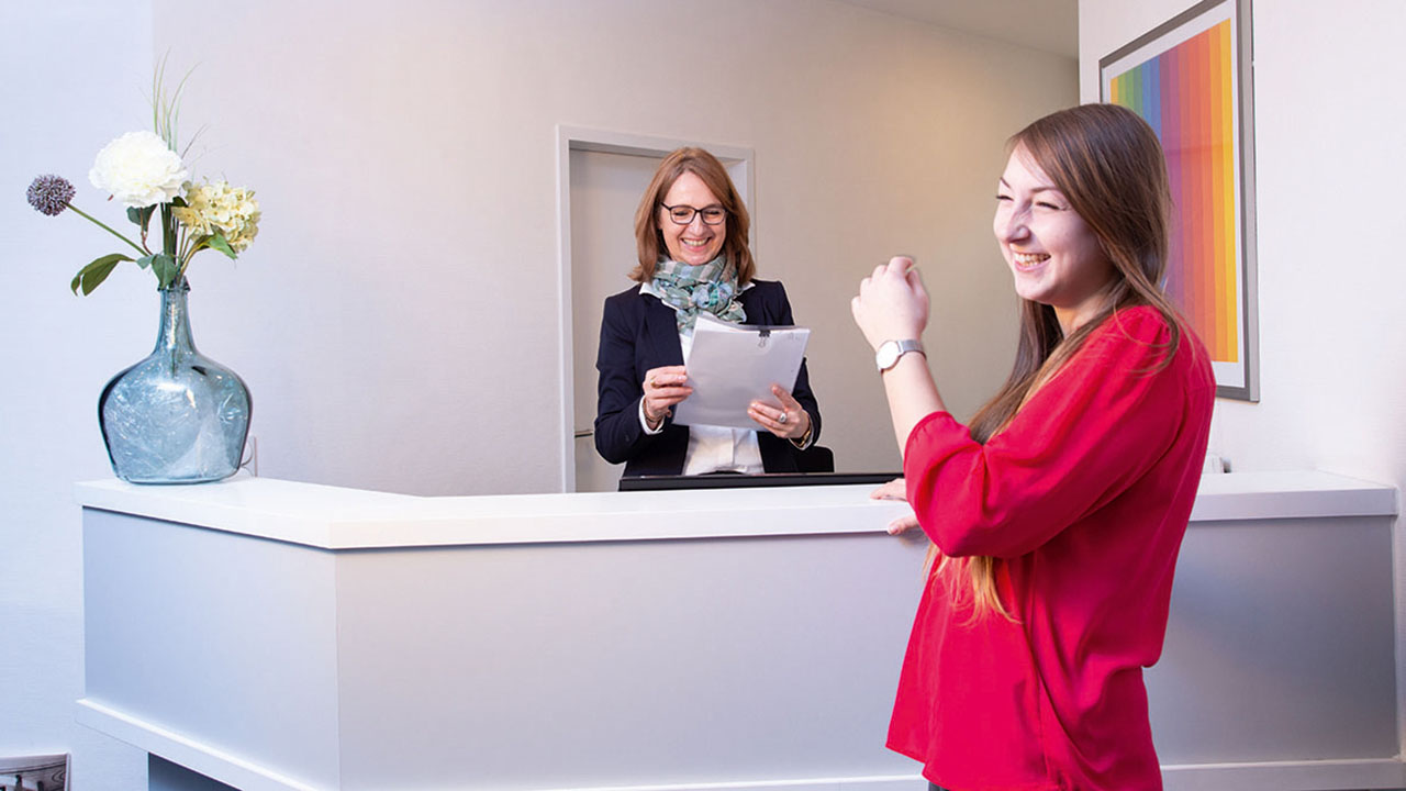 Zwei lachende Personen, eine vor und eine hinter dem Empfangstresen