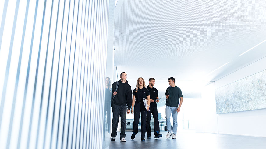 Vier Personen gehen gemeinsam durch einen hellen, modernen Flur und unterhalten sich.