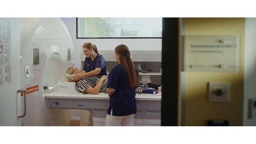 Zwei medizinische Fachangestellte bereiten eine Patientin auf eine radiologische Untersuchung im MRT-Gerät vor.