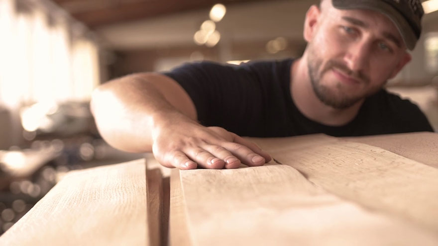 Handwerker in einer Werkstatt streicht mit der Hand über Holz.