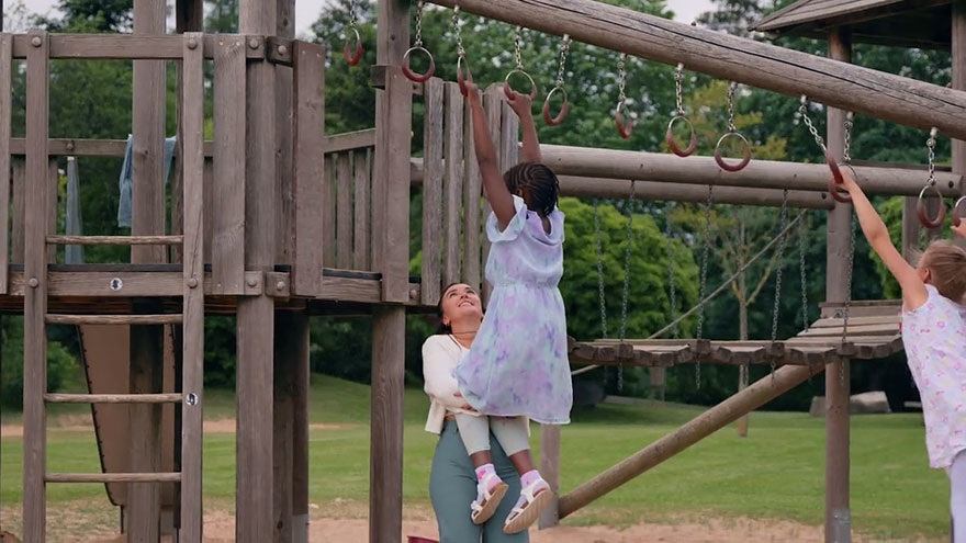 Klettergerüst im Freien. Betreuungskraft hilft einem Mädchen beim Klettern. 