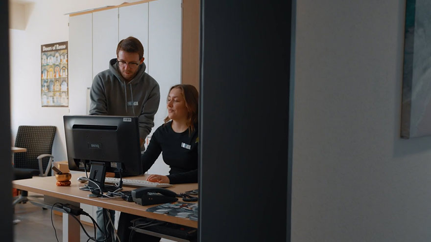 Studierende zusammen mit weiterer Person am Computer.