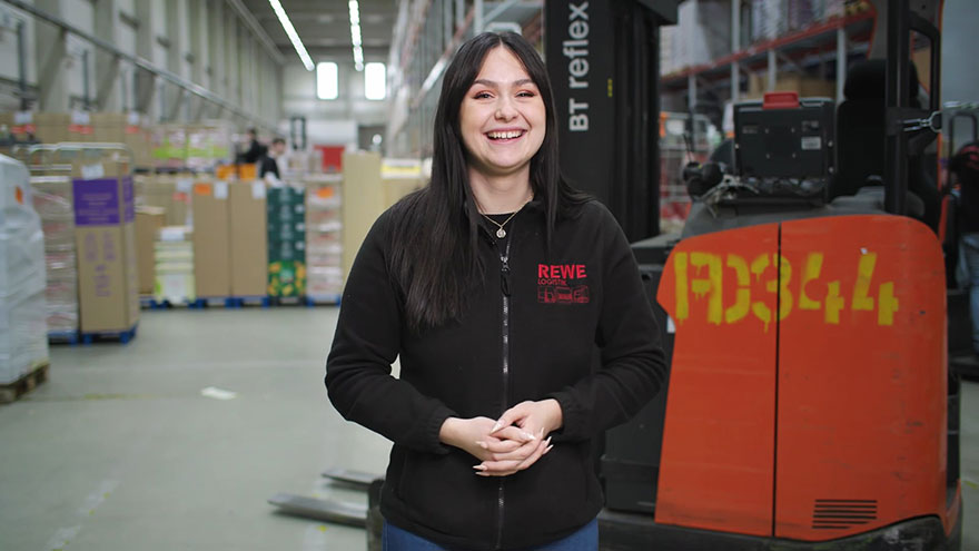 Auszubildende als Fachkraft für Lagerlostik vor Gabelstaplerim Lager der REWE Markt GmbH.
