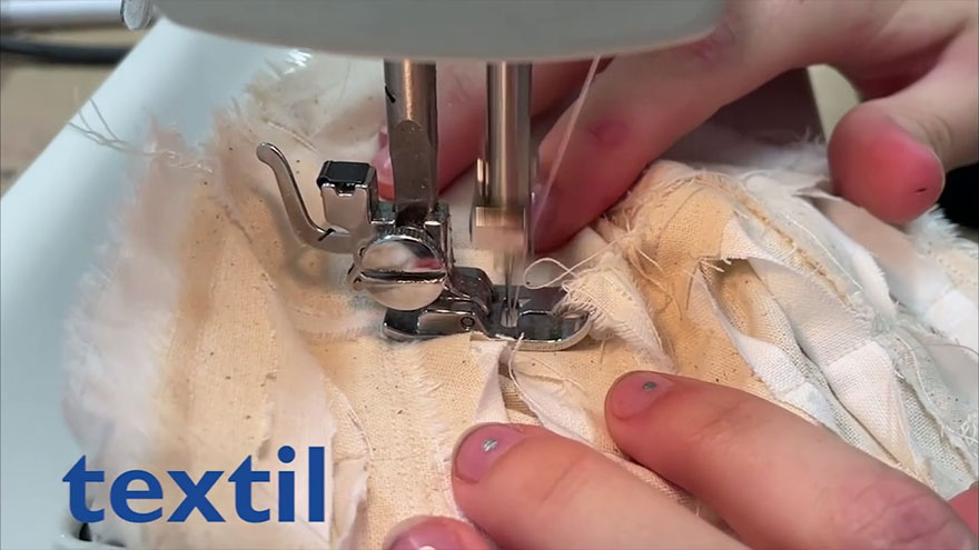 Nahaufnahme Nähmaschine: Hände führen Stoffstück unter den Nähfuß. 