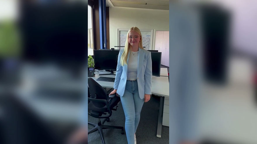 Auszubildende im Büro, vor einem Schreibtisch stehend.