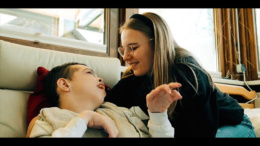 Heilerziehungspflegerin widmet sich einer assistenzbedürftigen Person, lächelt sie an.© Dominikus-Ringeisen-Werk