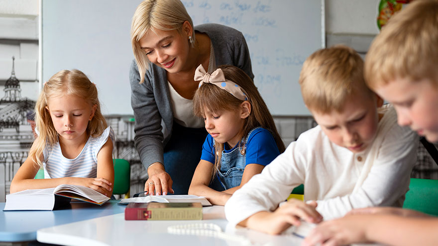 Lehrerin schaut Kindern in einer Schulklasse beim Lernen über die Schulter. © freepik